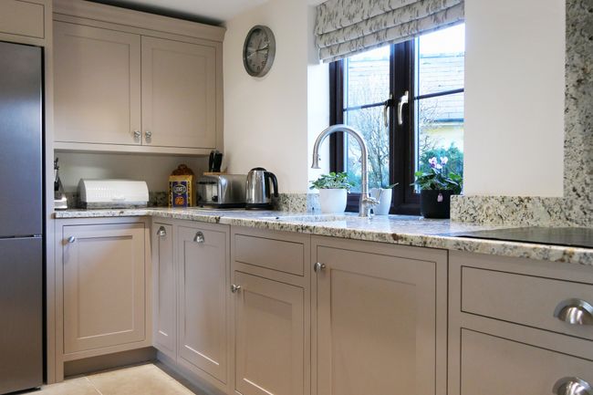 Shaker kitchen with beige cabinets and stainless steel appliances. Plants by a window add a touch of nature, with a calm, tidy ambiance.