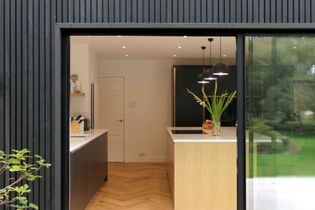 Modern kitchen with wooden island, black cabinets, white countertops, pendant lights, and a vase with flowers on the island.