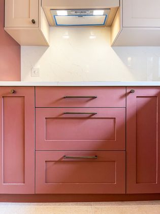 A close-up of kitchen cabinetry featuring a red drawers, with modern handles, set against a light-colored countertop and wall.