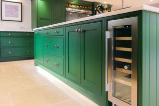 Shaker kitchen with vibrant green cabinetry, stainless steel wine cooler, and light beige tile flooring, creating an elegant, contemporary atmosphere.
