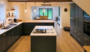 Dark cabinet Shaker kitchen with and island, pendant lights, a dining area, and glass doors opening onto a green lawn.