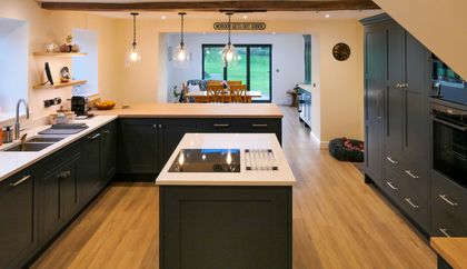 Shaker kitchen with dark cabinetry, a white island and countertops, glass pendant lights, exposed beams, and a sink beneath a window.