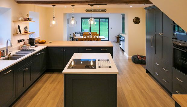 Shaker kitchen with dark cabinetry, a white island and countertops, glass pendant lights, exposed beams, and a sink beneath a window.