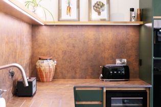 A modern kitchen with green cabinetry, a stainless steel sink, a toaster, a wine refrigerator, and wall art featuring vegetables.