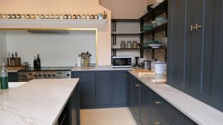 Spacious kitchen with dark grey cabinets, light worktops, and open shelving. Spices line a shelf above the stove. The atmosphere is modern and organized.