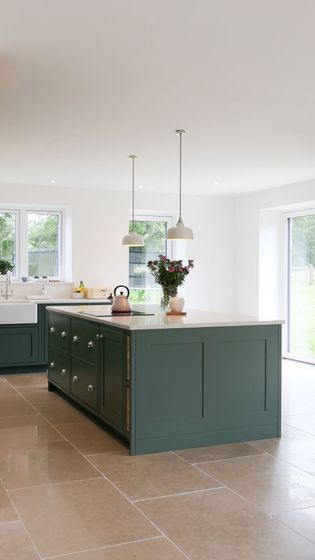 A spacious kitchen with a large green island, quartz worktop, and pendant lights. A vase of flowers and a kettle sit on the island, enhancing its modern, fresh feel.