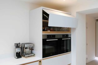 Modern kitchen with a built-in double oven, open upper cabinet revealing glassware, and a stainless steel espresso machine on the counter to the left.