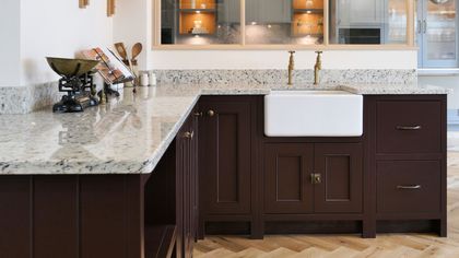 Deep burgundy Shaker kitchen with a butler sink, speckled granite worktop and brass taps