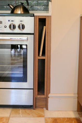 Kitchen corner with a stainless-steel range, kettle, narrow wooden shelf, and tiled floor.