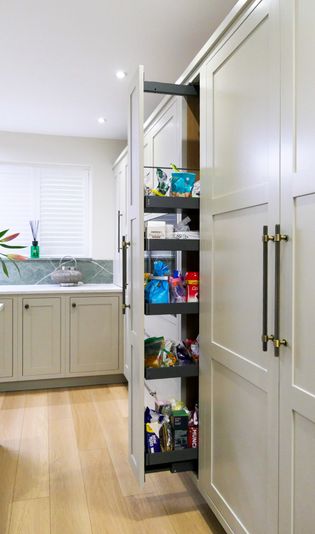 A kitchen pantry with shelves filled with various snacks and food items, integrated into cabinetry with a narrow opening to access the contents.