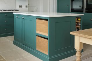 Green kitchen island with a white worktop, featuring wooden open shelves. The island is set on beige tile flooring in a welsh kitchen.