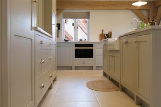 Spacious kitchen with neutral cabinets, a farmhouse sink, and wooden beams. Natural light streams through the window.