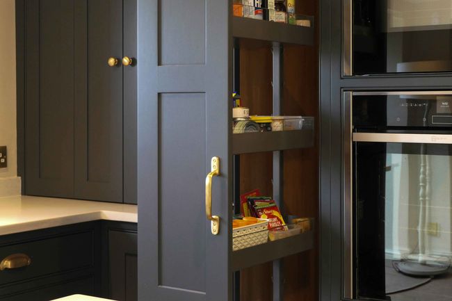 A dark grey kitchen cabinet with a pull-out pantry features organised shelves of canned goods and snacks. 