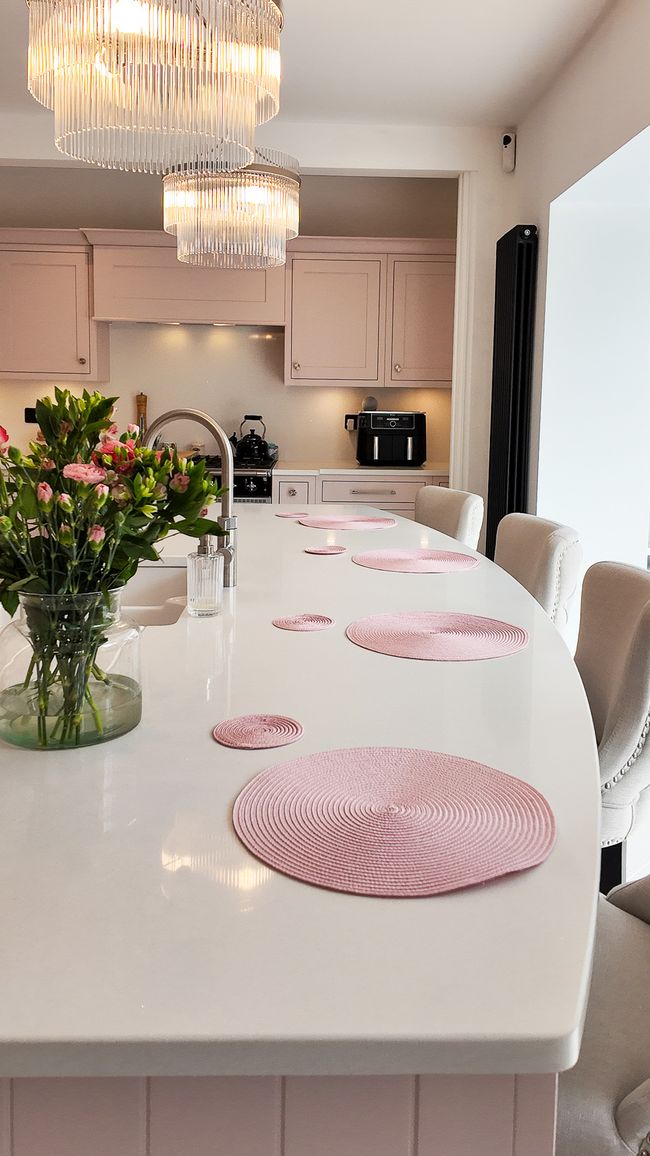 Large curved island with bar stools, pink placemats and pink bunch of flowers on the white worktop.