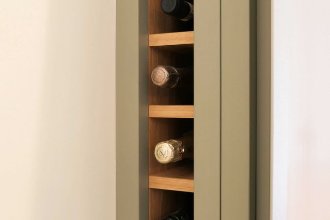 A small wooden wine rack with a beige frame houses several wine bottles laid horizontally. The minimalist design conveys elegance and order.