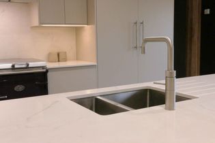 Modern kitchen interior featuring a stainless steel tap and sink set in a smooth, light-colored countertop. Minimalist cabinets and elegant handles emphasize a sleek, contemporary design.