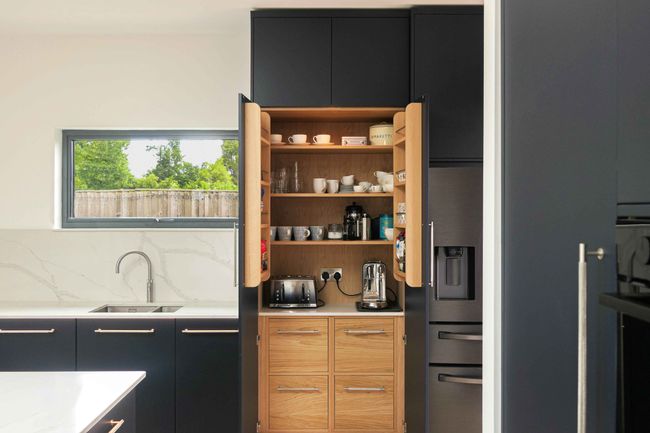 a handcrafted bespoke modern kitchen painted in a deep blue colour featuring an oak larder cupboard