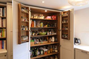 Well-organized pantry with jars of grains, spices on doors, and various food items on wooden shelves. Bright lighting creates a cozy, inviting atmosphere.