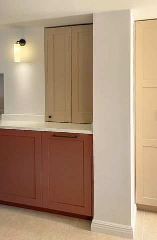 A Shaker kitchen featuring cabinets in two colours: red and a light beige, with a neutral wall and a light fixture.