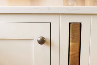 Close-up of a cream cabinet. A rustic, textured cutting board is partially visible in a vertical slot beside a round knob.