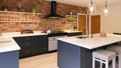 Bright kitchen with exposed brick walls, dark cabinetry, white countertops, a central island, open shelves, and pendant lights.
