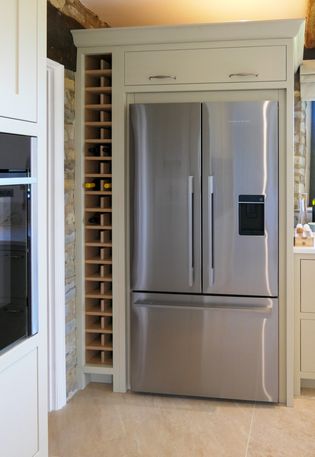 A stainless steel refrigerator with a wine rack next to it in a Shaker kitchen.
