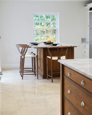 Elegant shaker kitchen with light worktops, walnut cabinetry, and 2 islands. Tall chairs and a large window create a bright, airy feel.