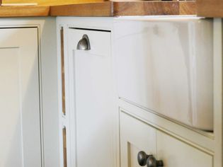 Close-up of a white kitchen cabinet with a farmhouse sink and wooden countertop. The cabinet has metal knobs, creating a warm, rustic feel.