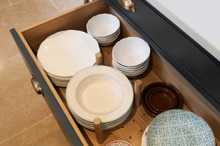 Open kitchen drawer with neatly arranged dishes and bowls, separated by wooden pegs. Plates are white and patterned, creating an organised, tidy look.