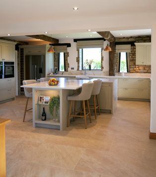 A Shaker kitchen featuring a large island with seating, light-coloured cabinets, and a spacious layout with natural light coming through the windows.