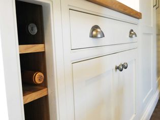 White kitchen cabinet with silver handles, wooden countertop, and three wooden wine racks on the side holding bottles. Modern and organized.