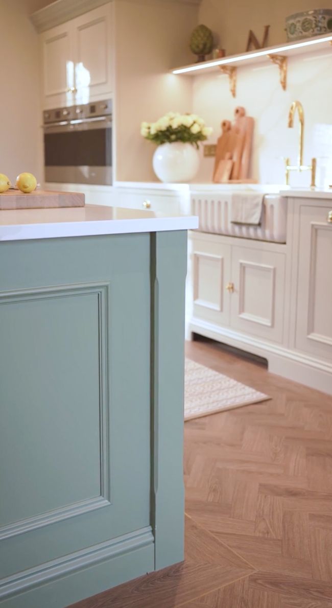 A Shaker kitchen featuring a light green island with a white countertop, a beautiful sink area with gold fixtures, and wooden accents on the floor.
