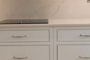 Shaker kitchen with white cabinets featuring silver handles, a sleek black induction cooktop, and marble-patterned backsplash, creating an elegant tone.