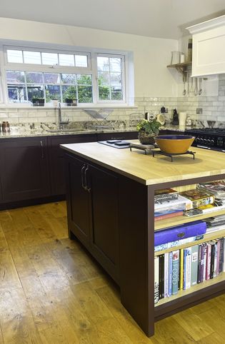 A Shaker kitchen featuring a wooden island with an open shelf displaying cookbooks, dark cabinetry, and a granite splashback.