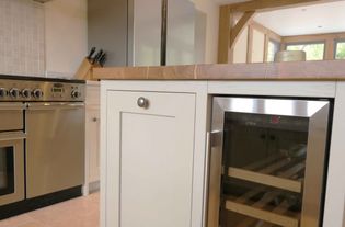 Shaker kitchen interior with stainless steel appliances, cream cabinetry, and a wood countertop. A wine fridge has been integrated into the island.