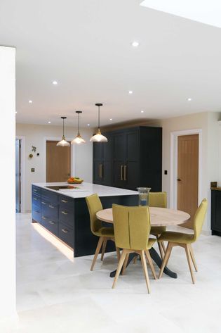 Shakerkitchen with a beige floor, dark grey cabinets, and a white countertop. Four chairs surround a round wooden table, under warm pendant lights.