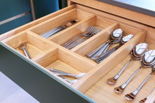A wooden cutlery drawer containing neatly arranged stainless steel forks, spoons, and knives.
