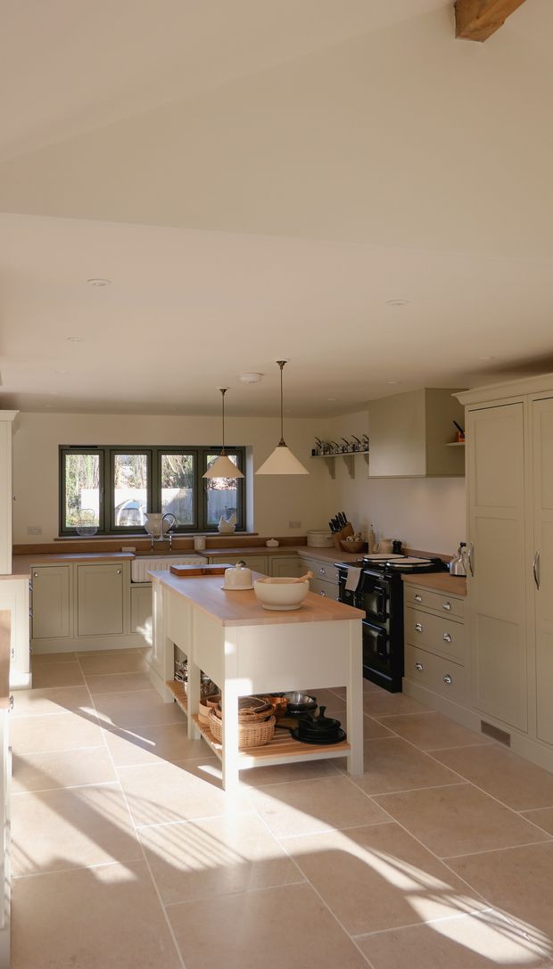 A Shaker kitchen with light-coloured cabinets, a large wooden countertop, a sink, and an AGA stove. There are utensils and kitchen tools neatly arranged, along with a window allowing natural light to fill the space.
