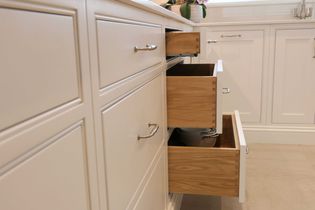 Kitchen drawers partially open, revealing light wood interiors and metallic handles. The surrounding cabinets are white, creating a clean, modern look.