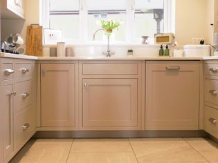 A shaker kitchen with neutral cabinets, white countertops, and a window above the sink. Fresh flowers and small kitchen items add a cozy, welcoming feel.