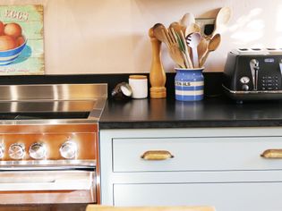A cozy kitchen scene featuring a shiny stainless steel oven, a blue utensil holder with wooden spoons, a black toaster, and a vintage egg sign on the wall.