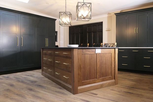 Shaker kitchen with dark cabinetry, a walnut island, brass hardware, wood flooring, and geometric pendant lights.