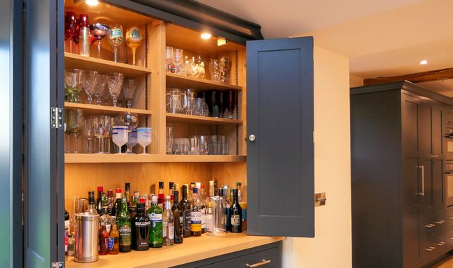 Open illuminated home bar stocked with glassware and liquor bottles within a large dresser.