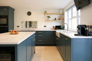 Shaker kitchen with teal cabinets, white countertops, and minimalist decor. A fruit bowl adds warmth, while ample natural light creates a welcoming tone.