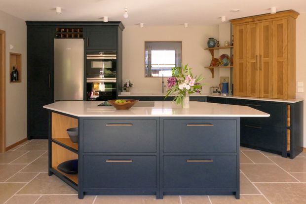 Shaker kitchen with a dark blue island, white countertops, wooden cabinetry, fruit bowl, and vase of flowers.