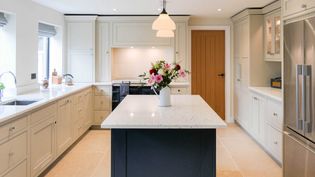 Bright kitchen with cream cabinets and a contrasting navy blue island topped with flowers in a vase. Shaker design, stainless steel appliances, and soft lighting.