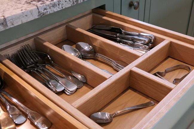 Open kitchen drawer with neatly organised cutlery in a wooden divider with forks, spoons, knives. Neutral green drawer front and marble countertop.