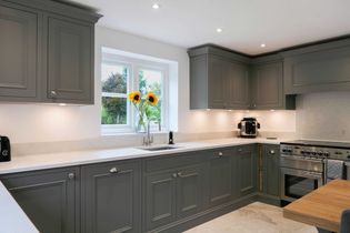 Shaker kitchen with sleek grey cabinetry and quartz worktop. A vase with sunflowers sits on the sink by the window. Stainless steel appliances gleam.