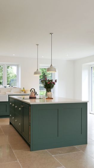 Shaker kitchen with a large green island, pendant lights, and beige floor tiles. A vase with flowers and a kettle sits on the island.
