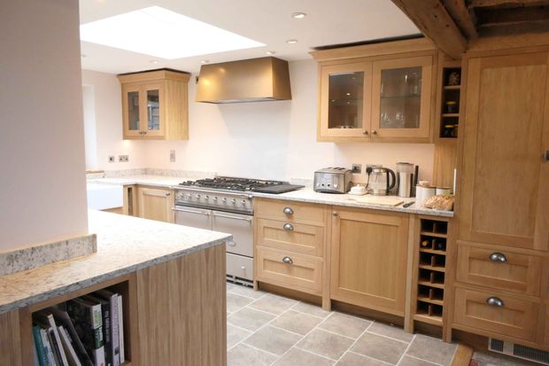 Shaker kitchen with light wood cabinets, stone countertops, a central range, and a foreground island with cookbooks.